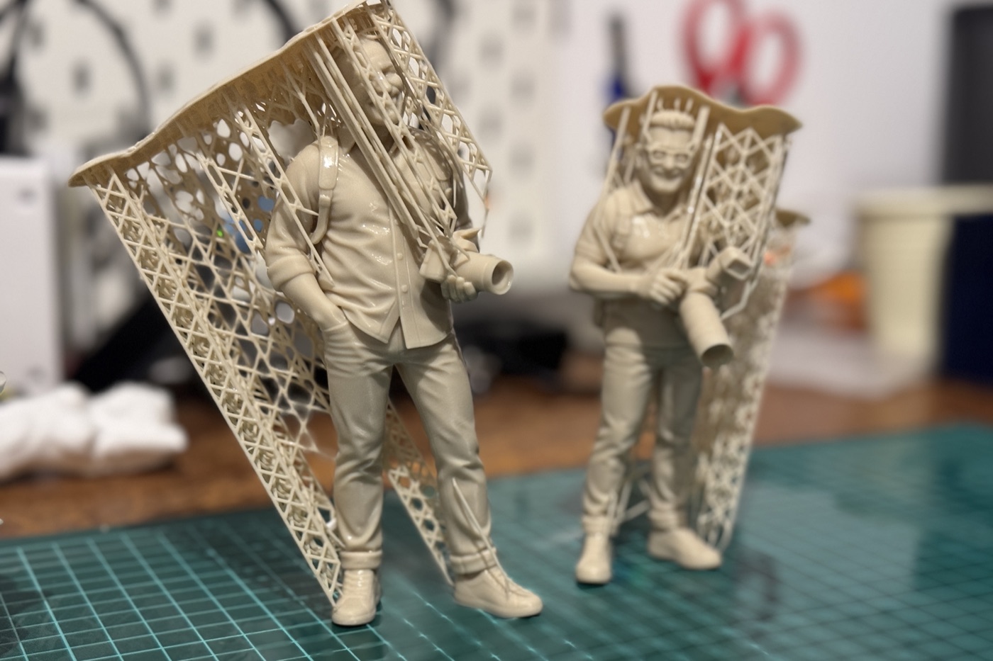 Deux figurines sortant de l'imprimante, leurs supports d'impression encore attachés