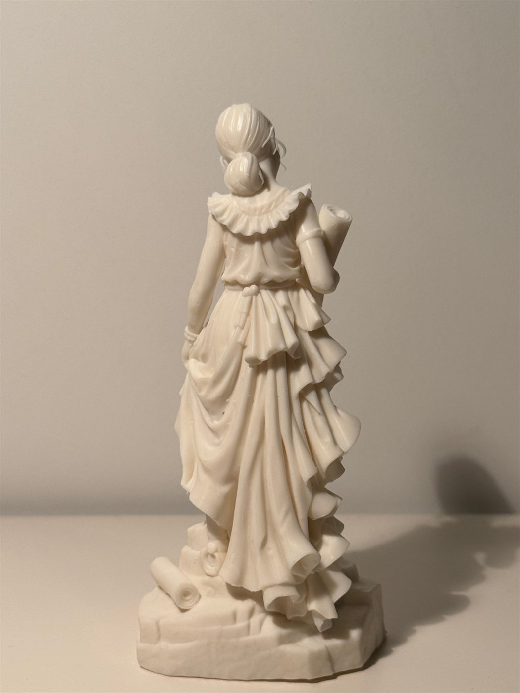 La statuette vue de dos : chignon, col à volants, ceinture nouée et traîne de la robe