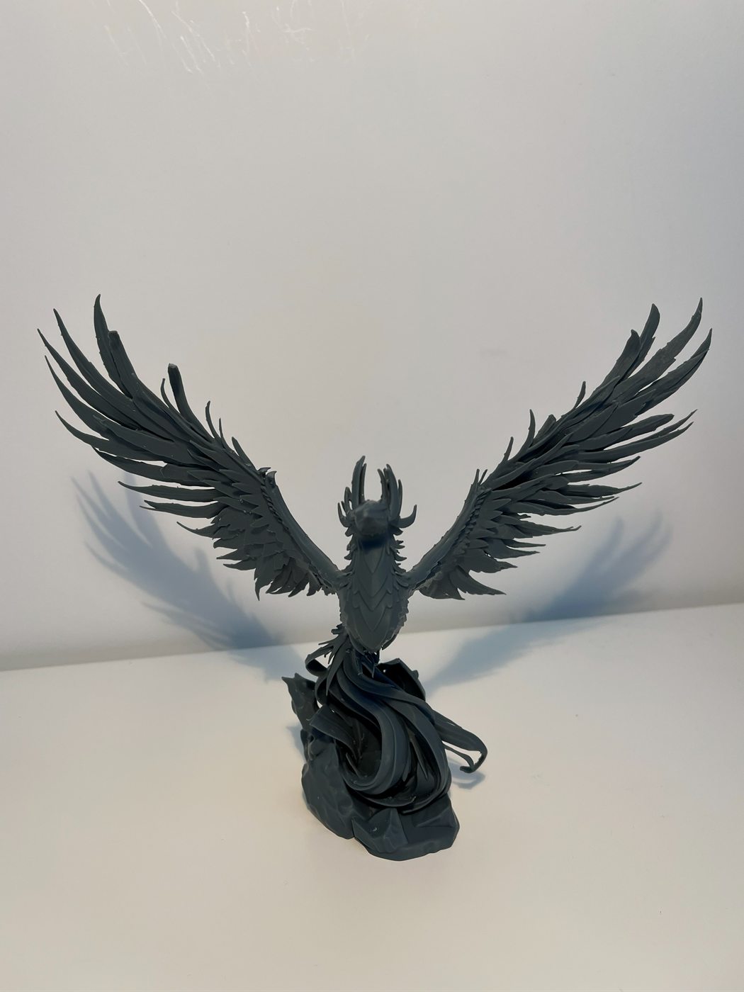 Sculpture d'un phénix en résine grise, ailes déployées, s'élevant d'un socle de flammes