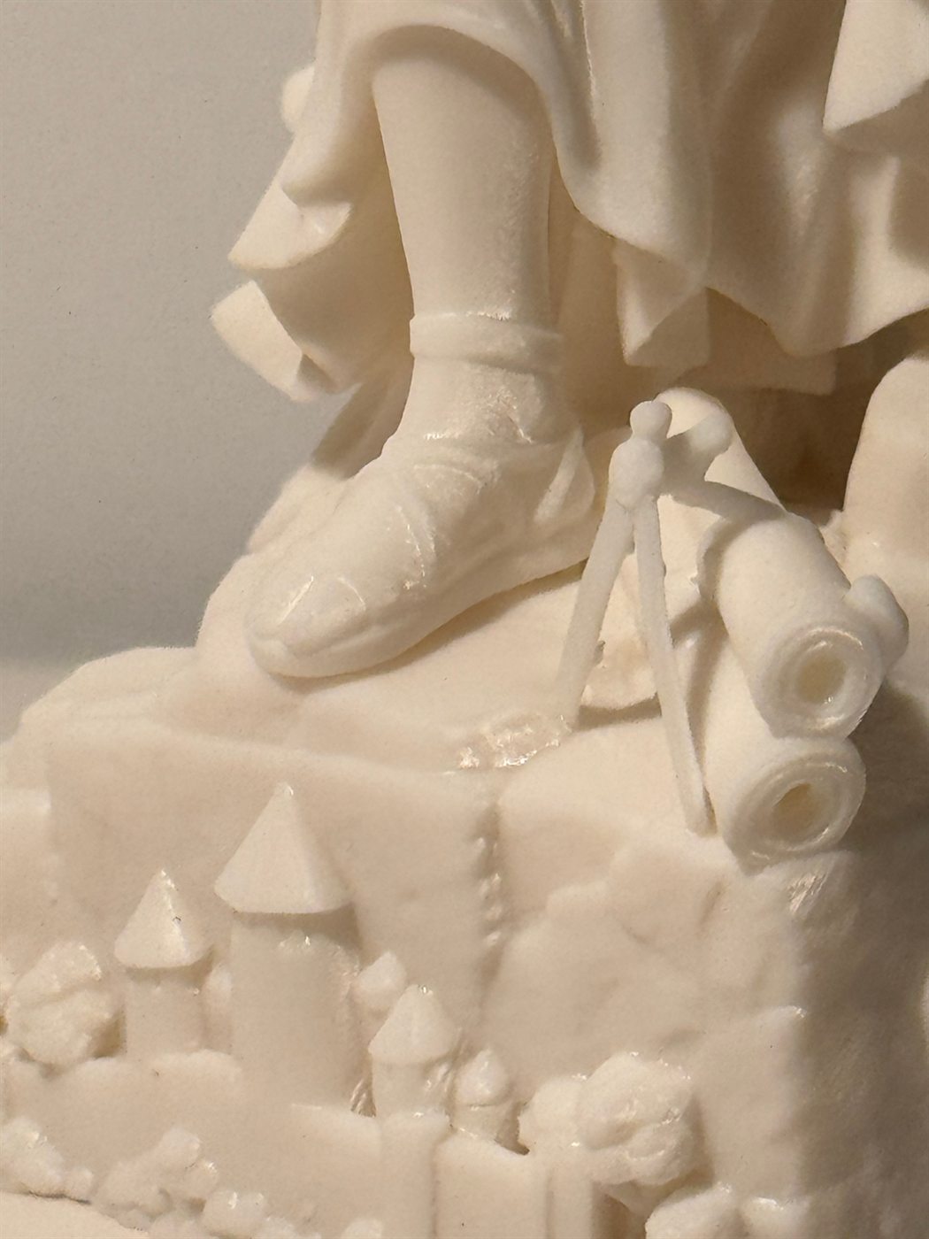 Détail du socle : sandale, compas, rouleaux de plans et cité fortifiée sculptée
