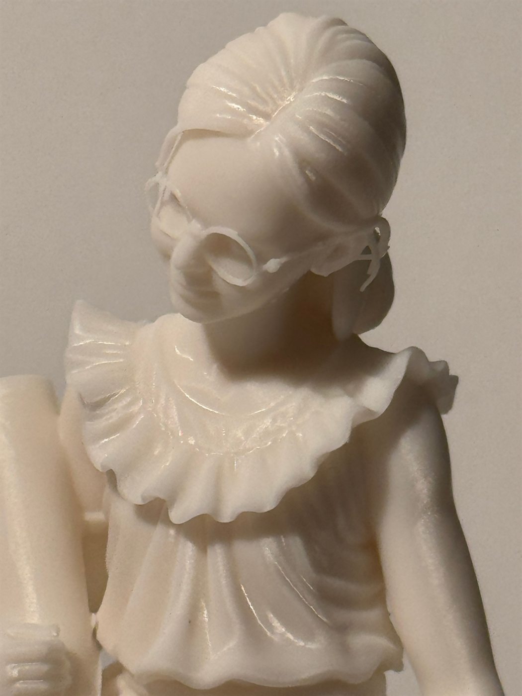 Détail du visage de la statuette : lunettes rondes, chignon, col à volants